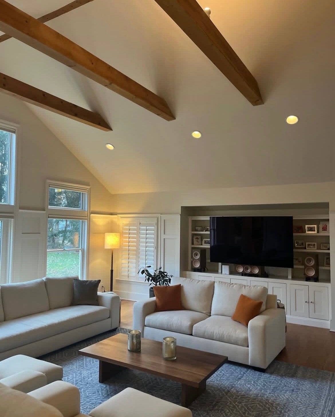 Great room with vaulted wood-beam ceiling, stone fireplace, and white seating